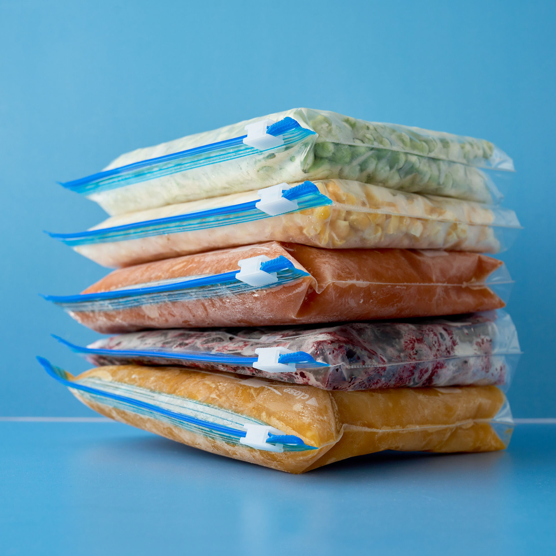 Gestapelte Toppits Zipper Beutel mit verschiedenen gefrorenen Lebensmitteln, luftdicht verschlossen, auf blauem Hintergrund