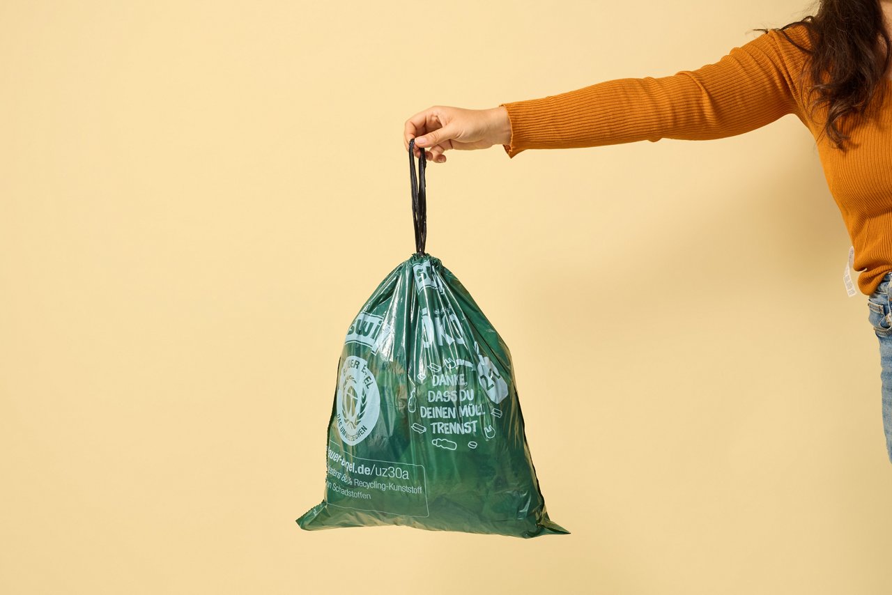 Hand hält gefüllten Swirl Öko Müllbeutel an Zugand ins Bild