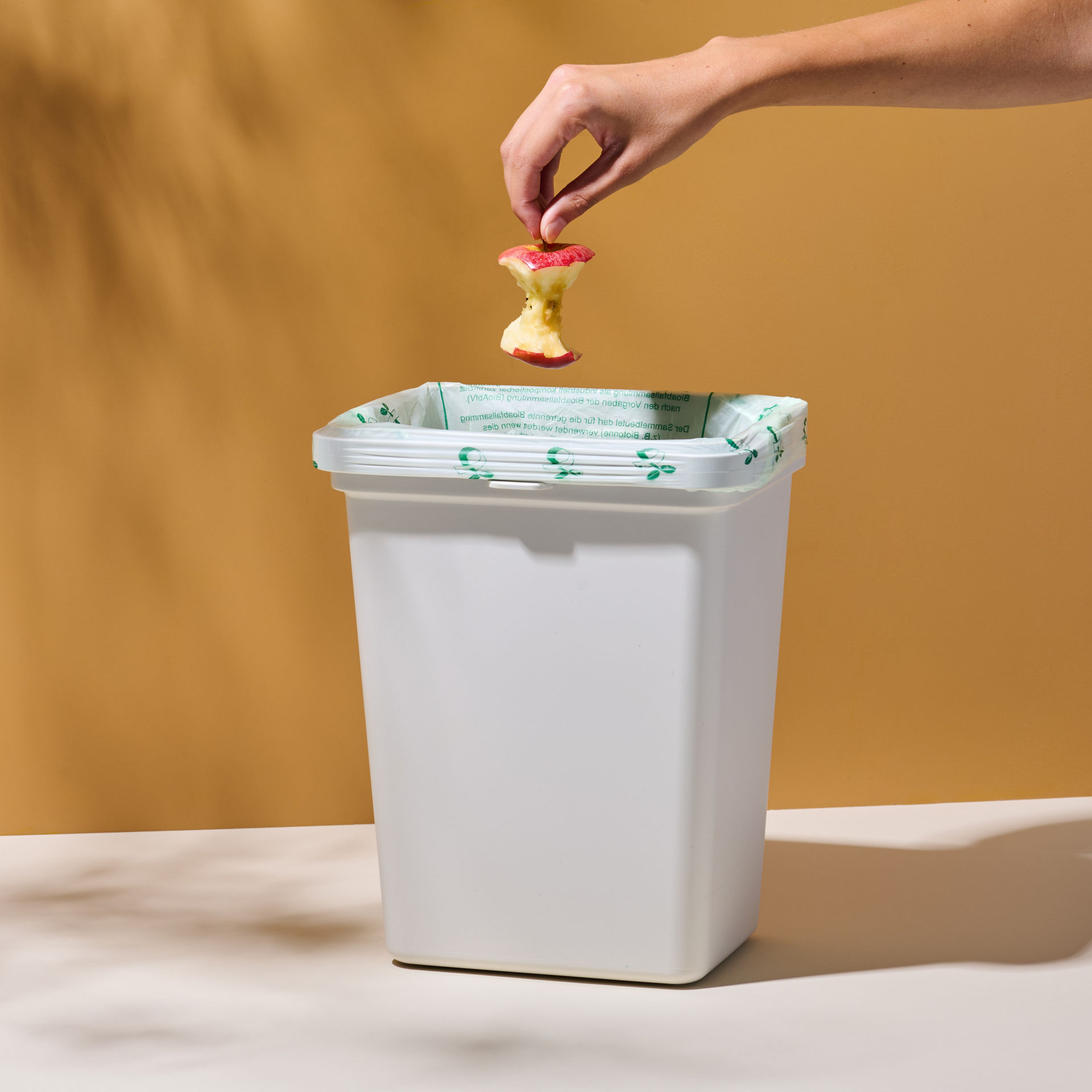 Hand wirft Apfelstrunk in Mülleimer mit wirl Bio-Müll Folienbeutel