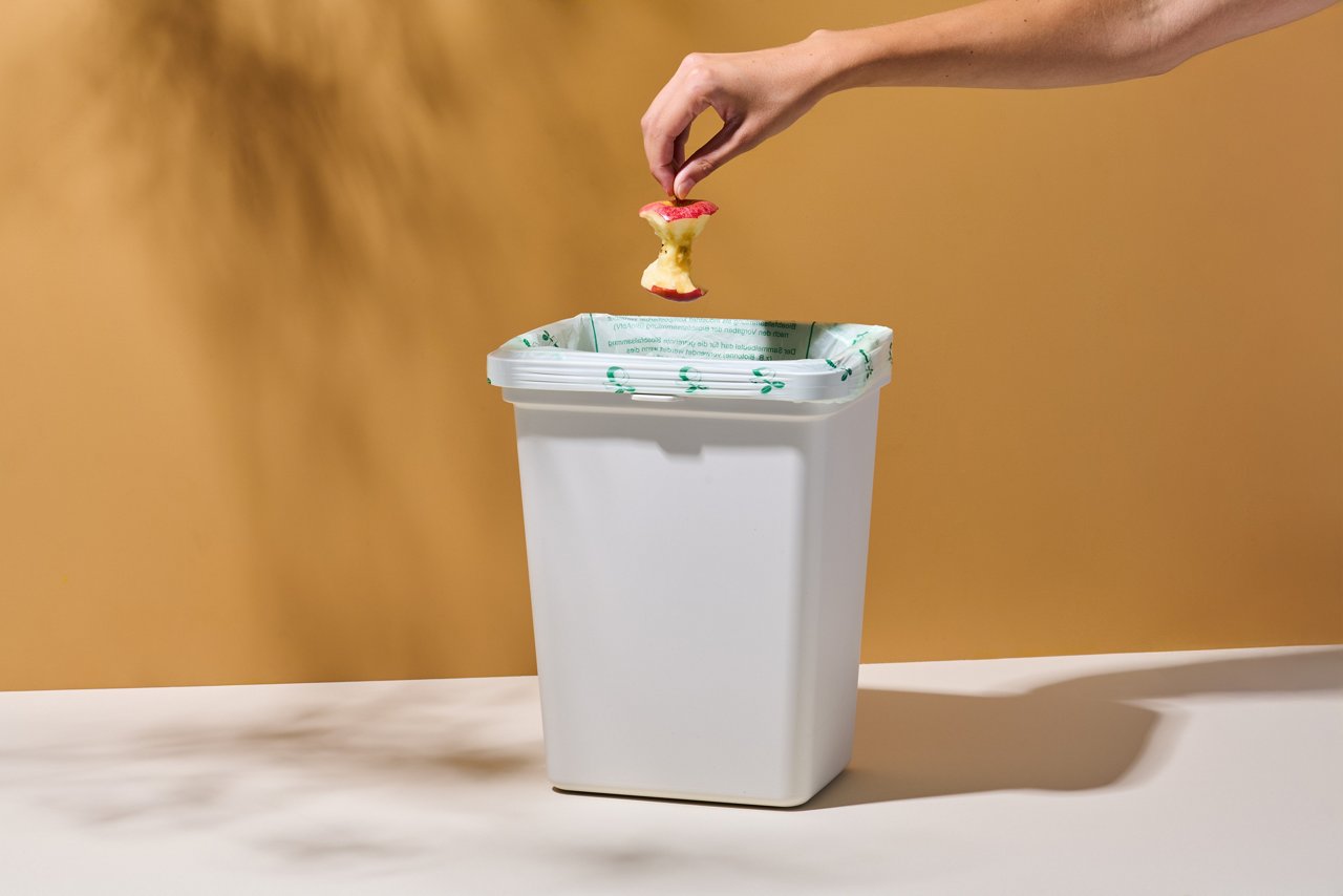 Hand wirft Apfelstrunk in Mülleimer mit wirl Bio-Müll Folienbeutel
