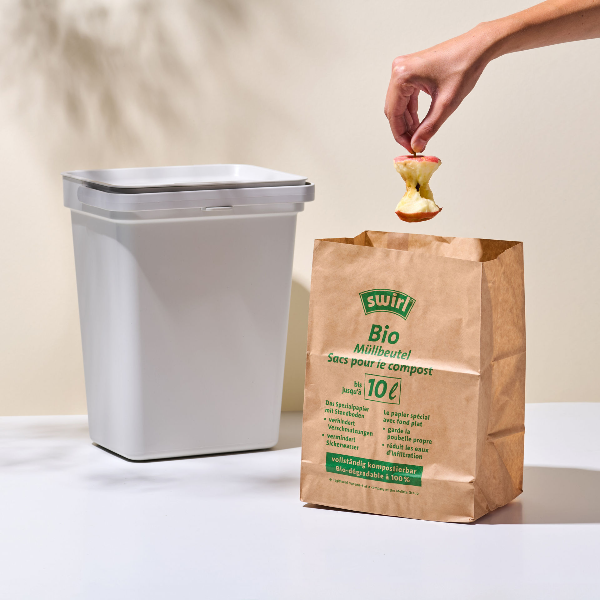 Apfelstrunk wird im Swirl Bio-Müll Papierbeutel vor Mülleimer stehend entsorgt