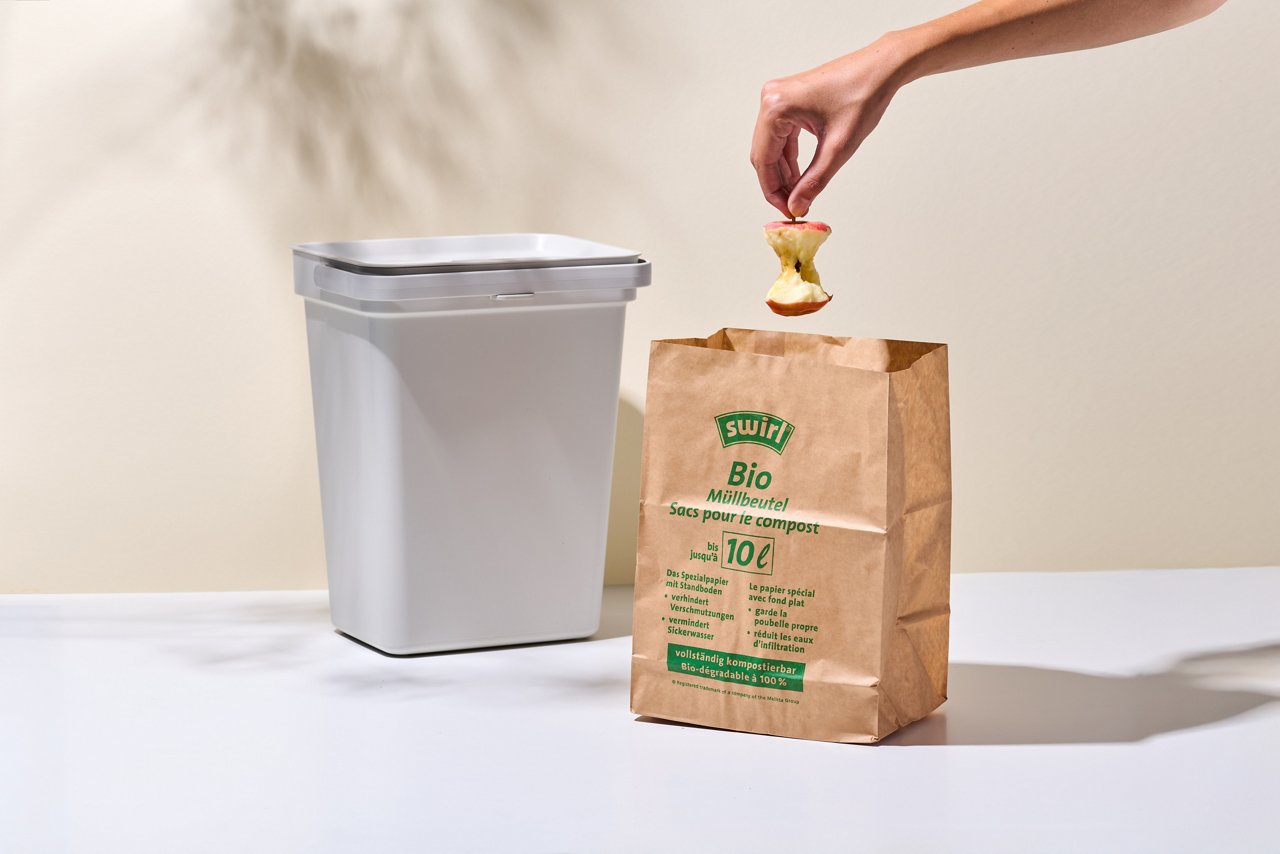 Apfelstrunk wird im Swirl Bio-Müll Papierbeutel vor Mülleimer stehend entsorgt