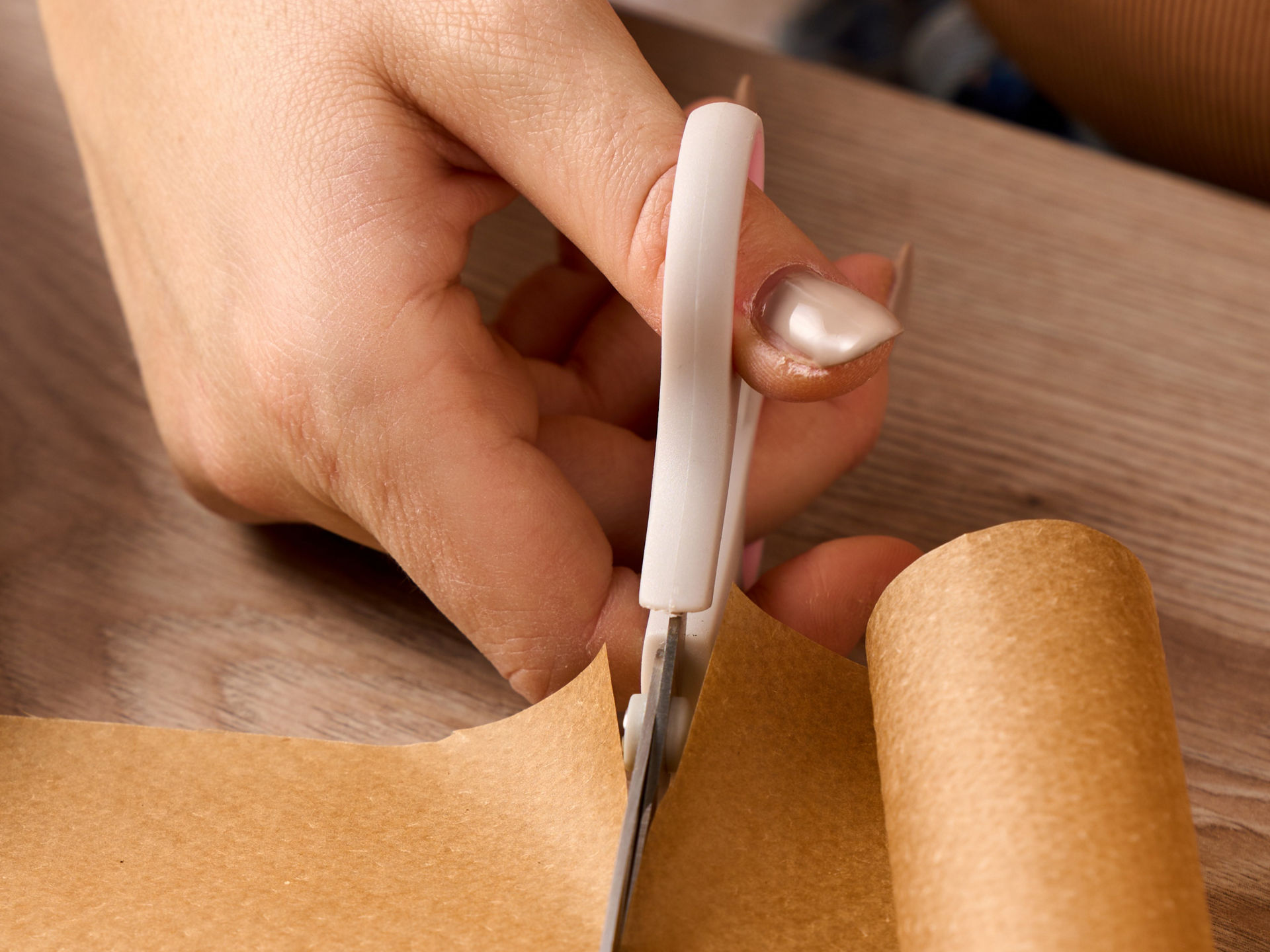 Eine Hand schneidet ein Stück braunes Toppits Backpapier mit einer Schere von einer Rolle ab.