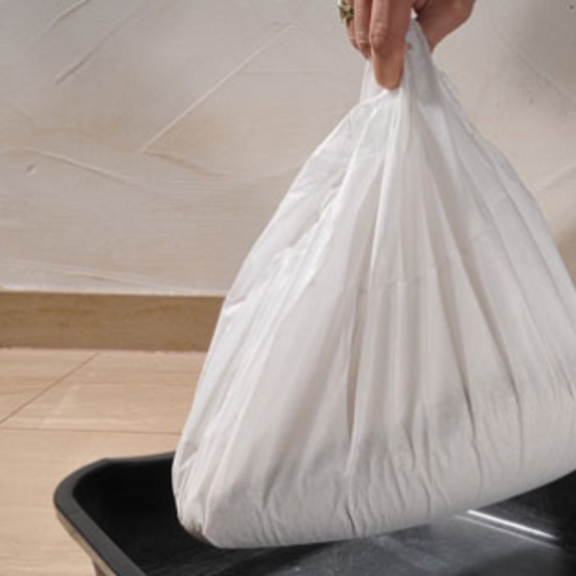 Personne refermant et soulevant le sac de protection rempli de litière au-dessus du bac à litière. 