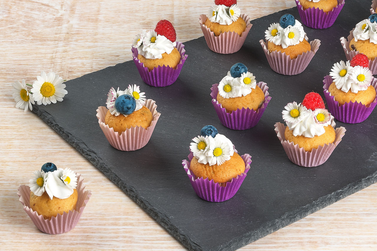 Flowe Muffings mit Gänseblümchen dekoriert stehen auf einer Schiefernplatte