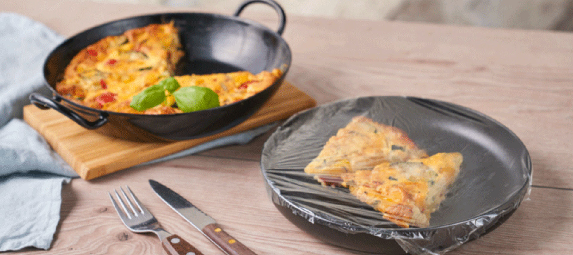 Ein Stück Frittata auf einem Teller, abgedeckt mit Toppits Frischhaltefolie. Daneben eine Pfanne mit der restlichen Frittata.