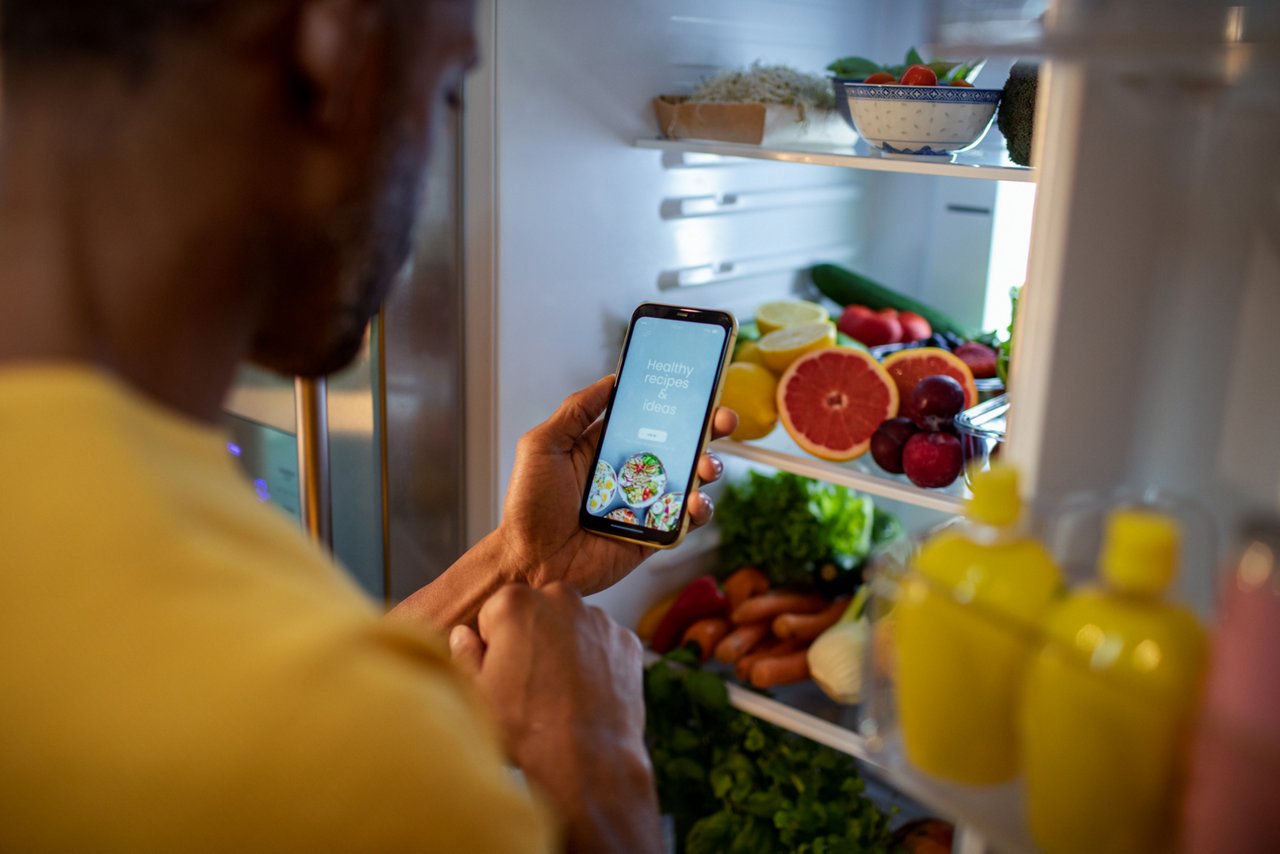 Middle aged african american man using a dieting app while looking through his fridge in the kitchen at home