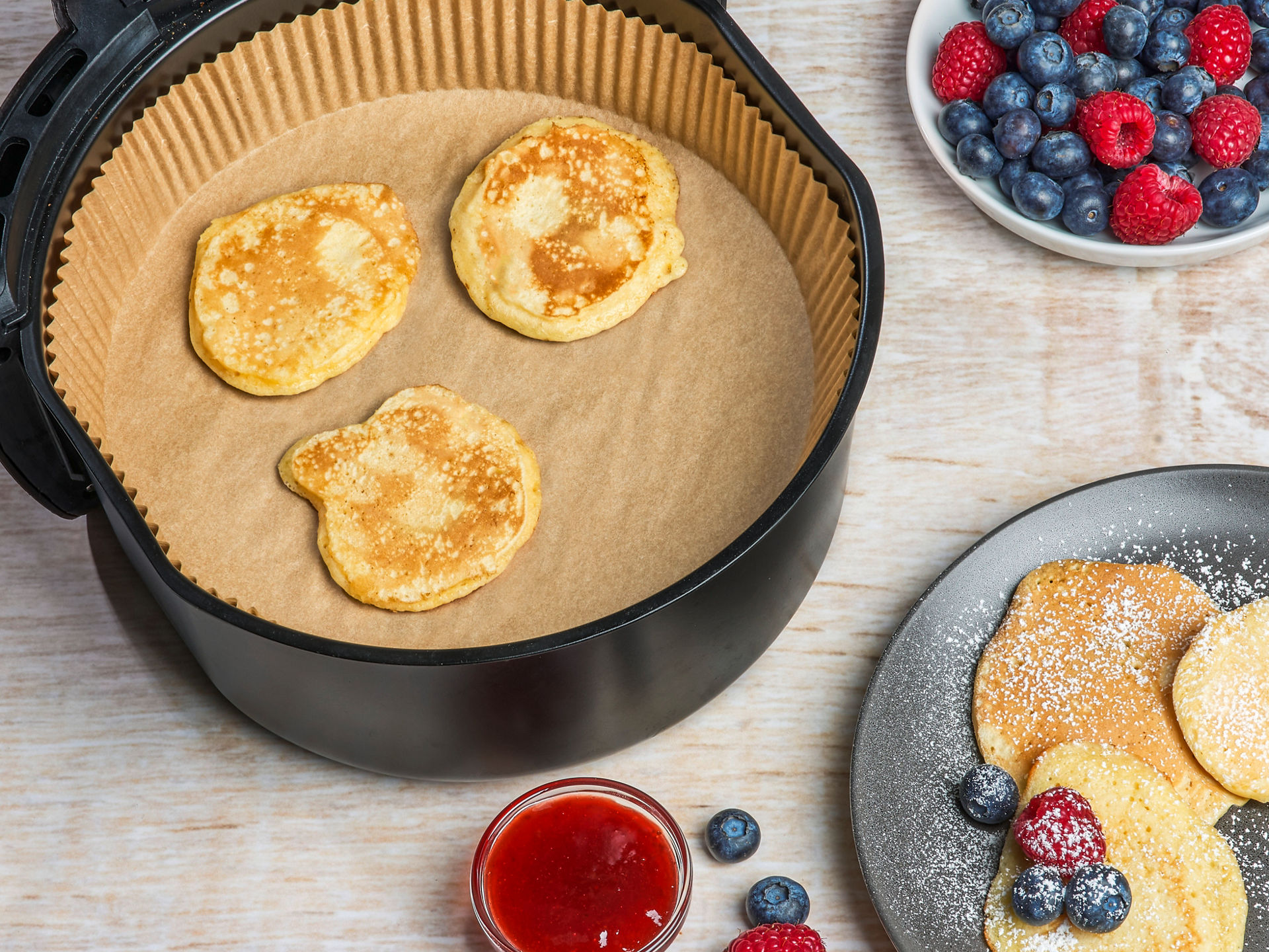 Frische Pancakes auf Toppits Backpapier in der Heißluftfritteuse, serviert mit Beeren und Puderzucker.