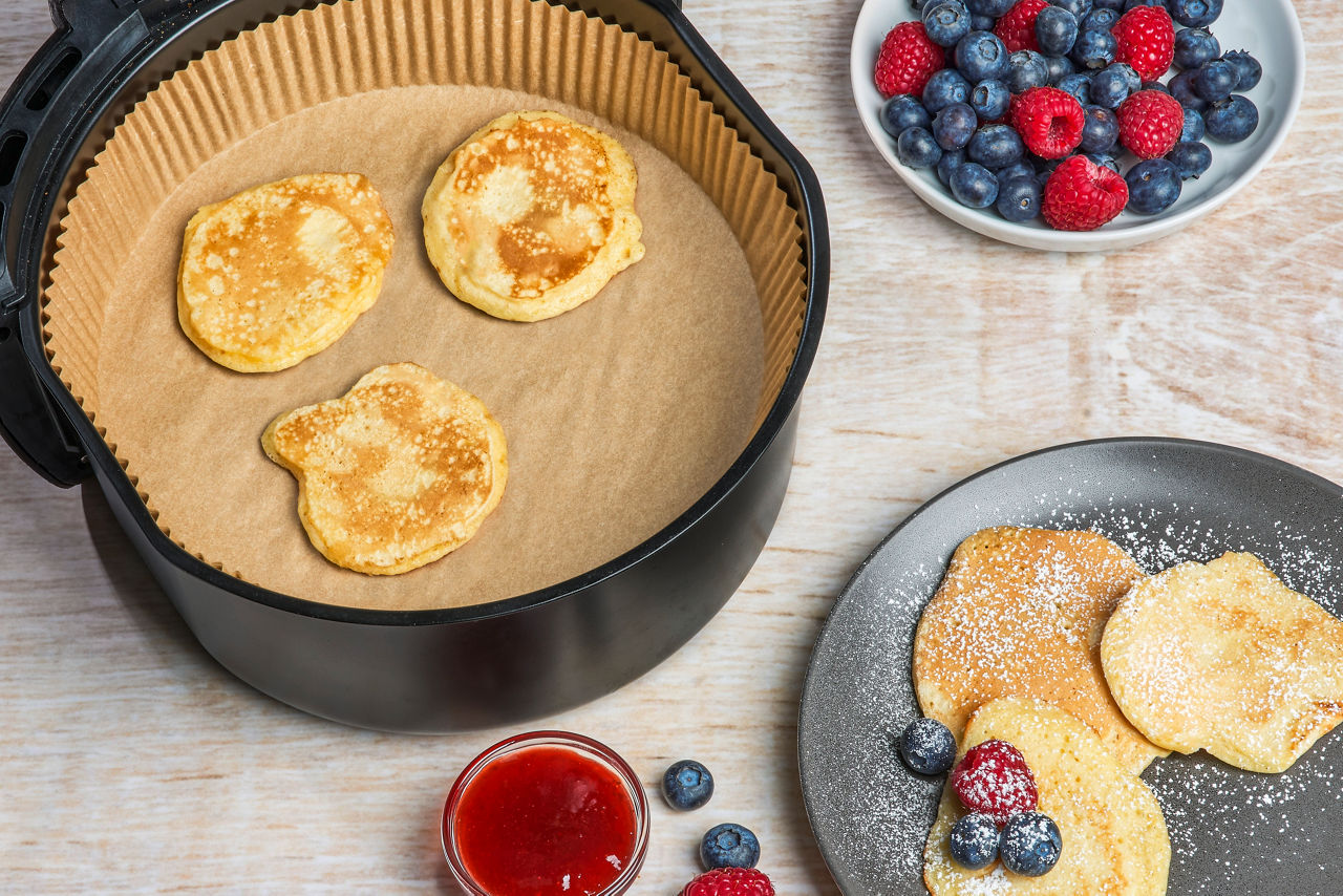 Frische Pancakes auf Toppits Backpapier in der Heißluftfritteuse, serviert mit Beeren und Puderzucker.