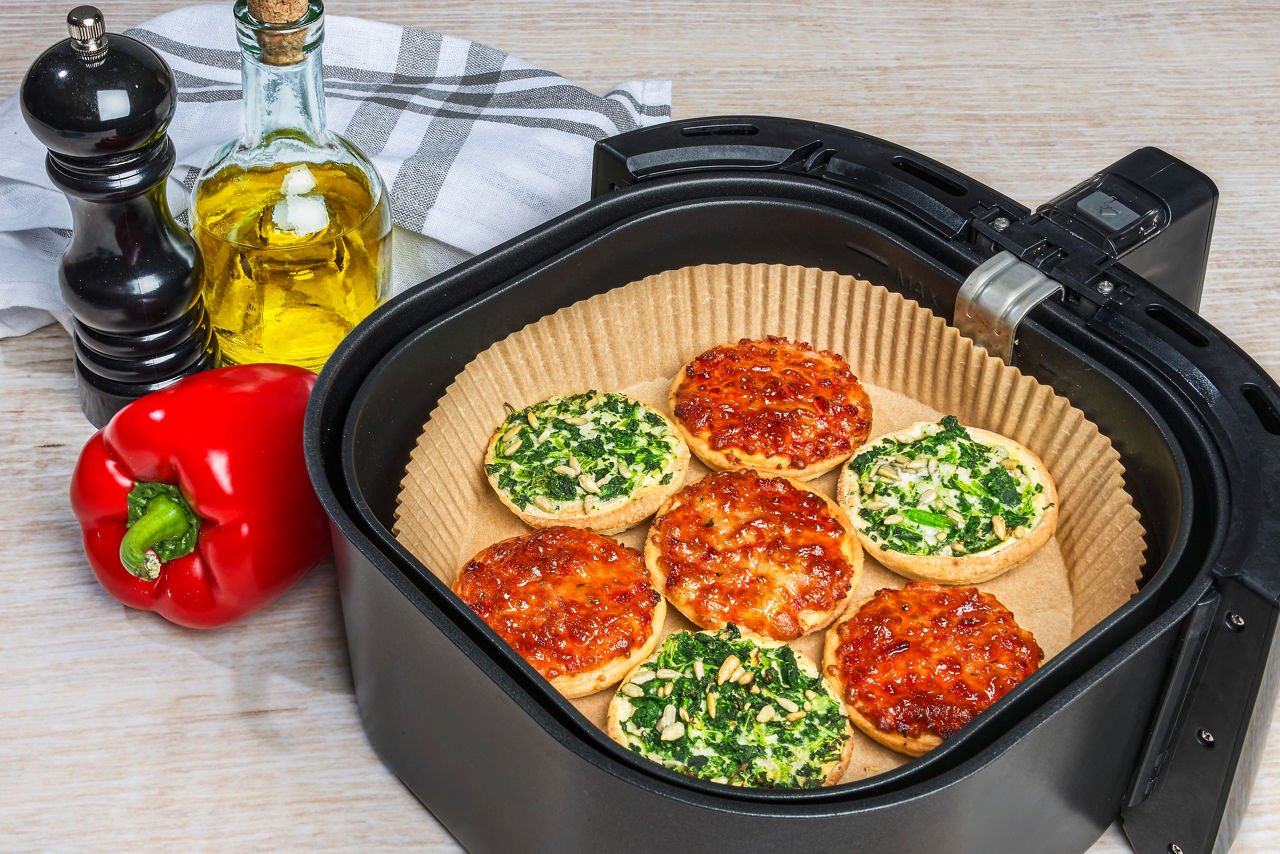 Mini-Pizzen mit Spinat und Tomate auf Toppits Backpapier in der Heißluftfritteuse, frische Zutaten.
