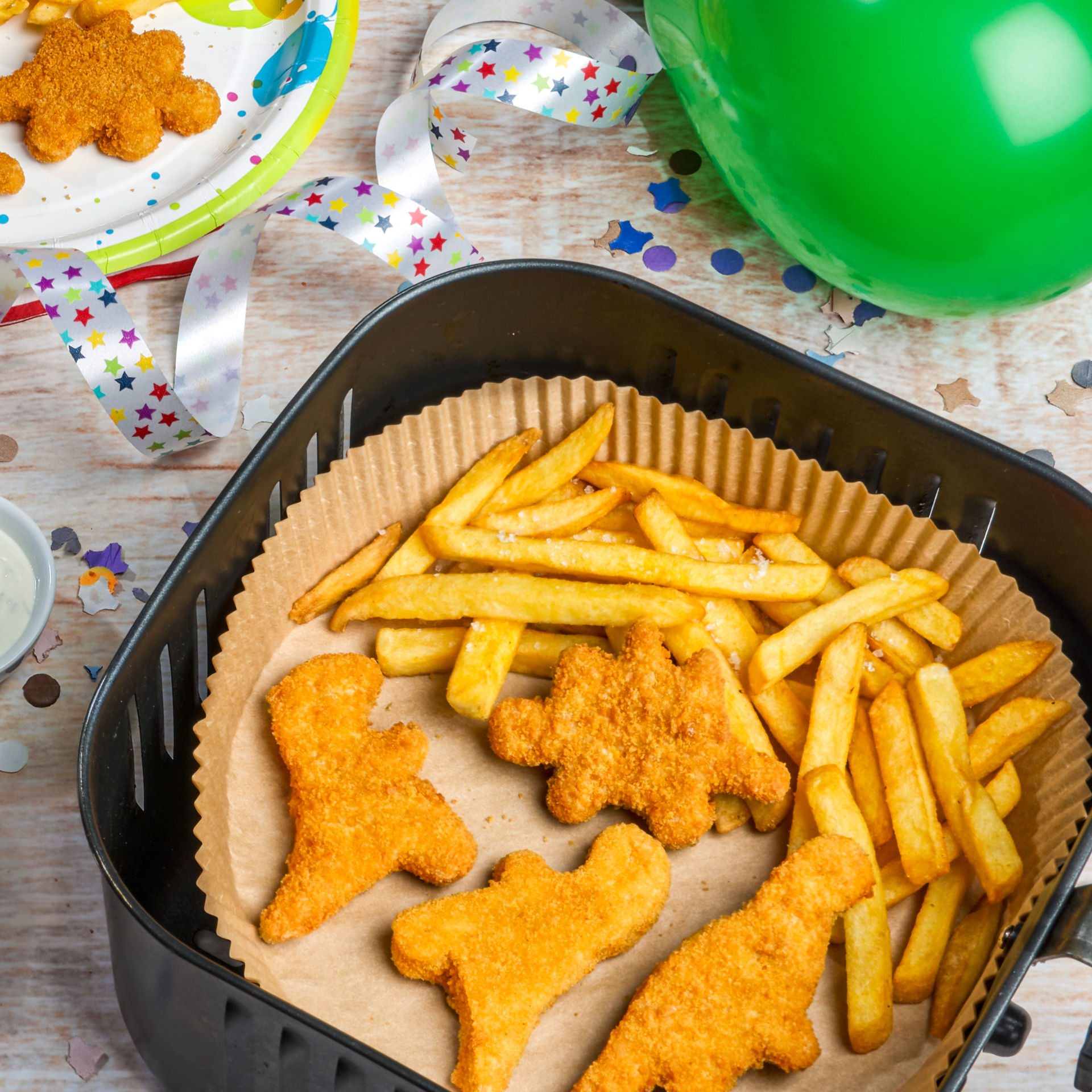 Pommes und Dino-Nuggets auf Toppits Backpapier in der Heißluftfritteuse, Partydekoration.