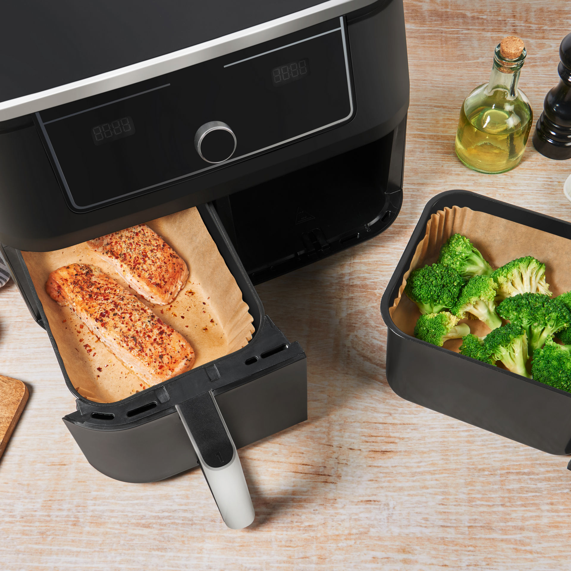 Freidora de aire con salmón y brócoli listos para cocinar, rodeada de ingredientes frescos.