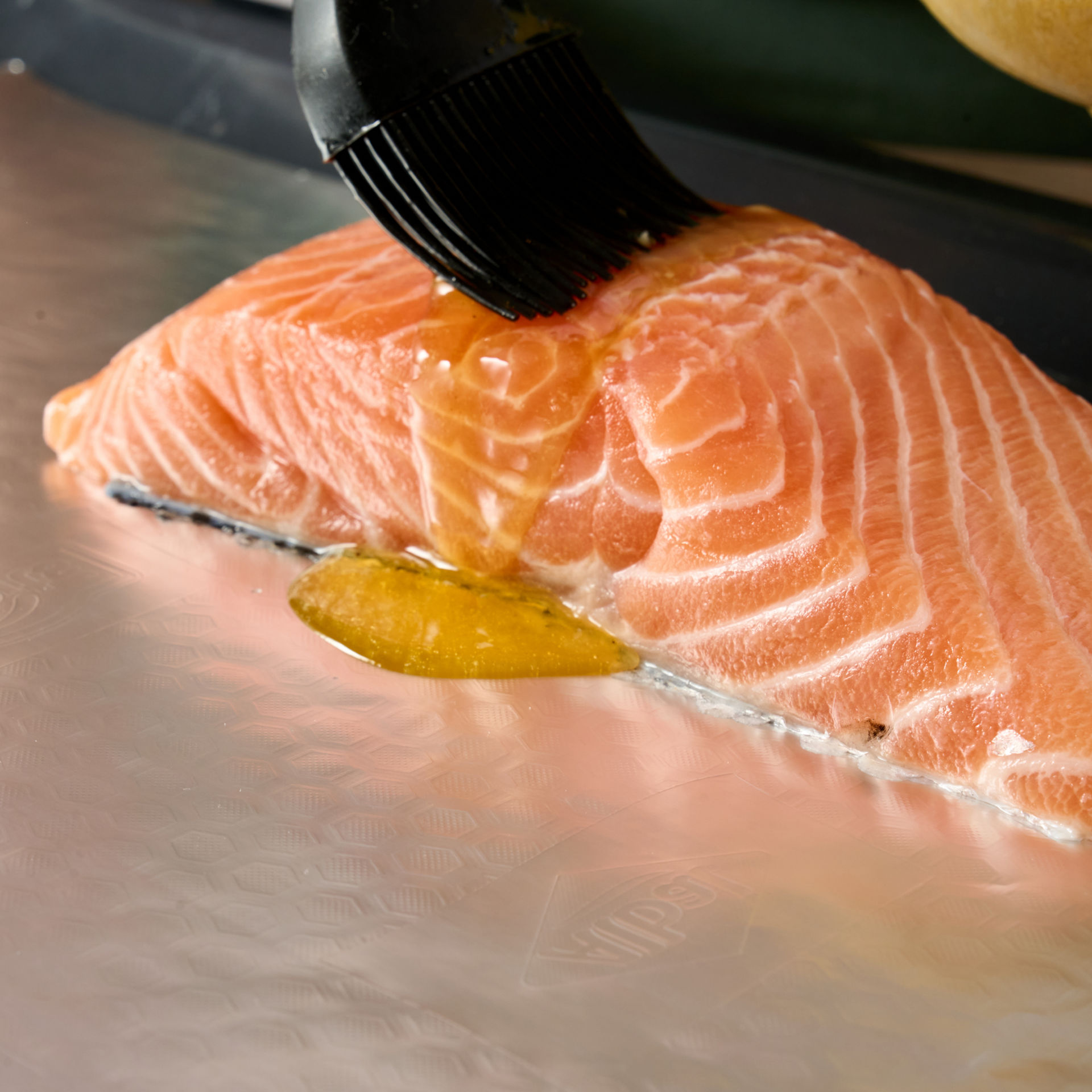 Pinceau badigeonnant d'huile un pavé de saumon sur du papier aluminium Albal