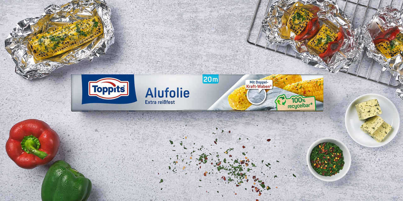 Toppits Alufolie mit gegrilltem Mais und Paprika auf einer Arbeitsfläche.