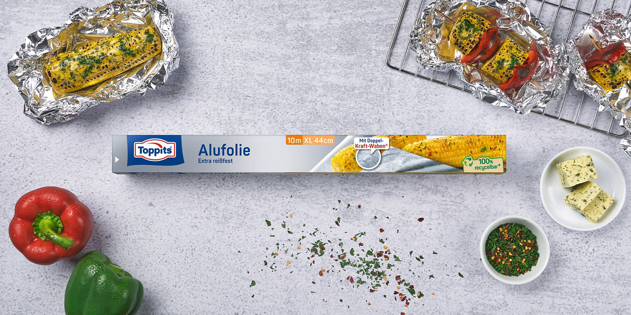 Toppits XL Alufolie mit gegrilltem Mais und Gemüse auf einer Arbeitsfläche.