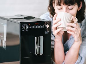 Aromatischer Kaffeegenuss (03)1.png – Melitta® Lifestyle – Woman sitting at table smiling with coffee mug in hand
