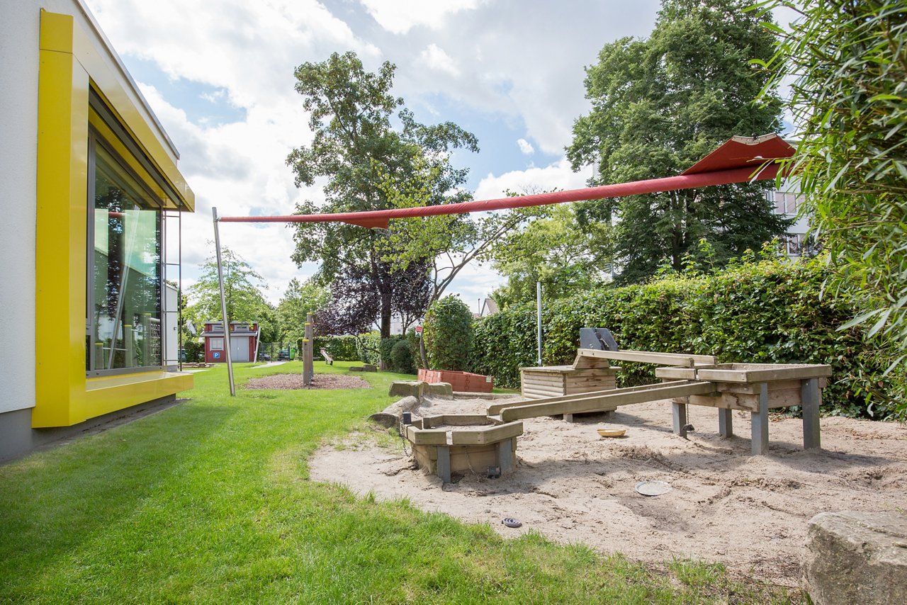 large, round sandpit with playground equipment and red awnings