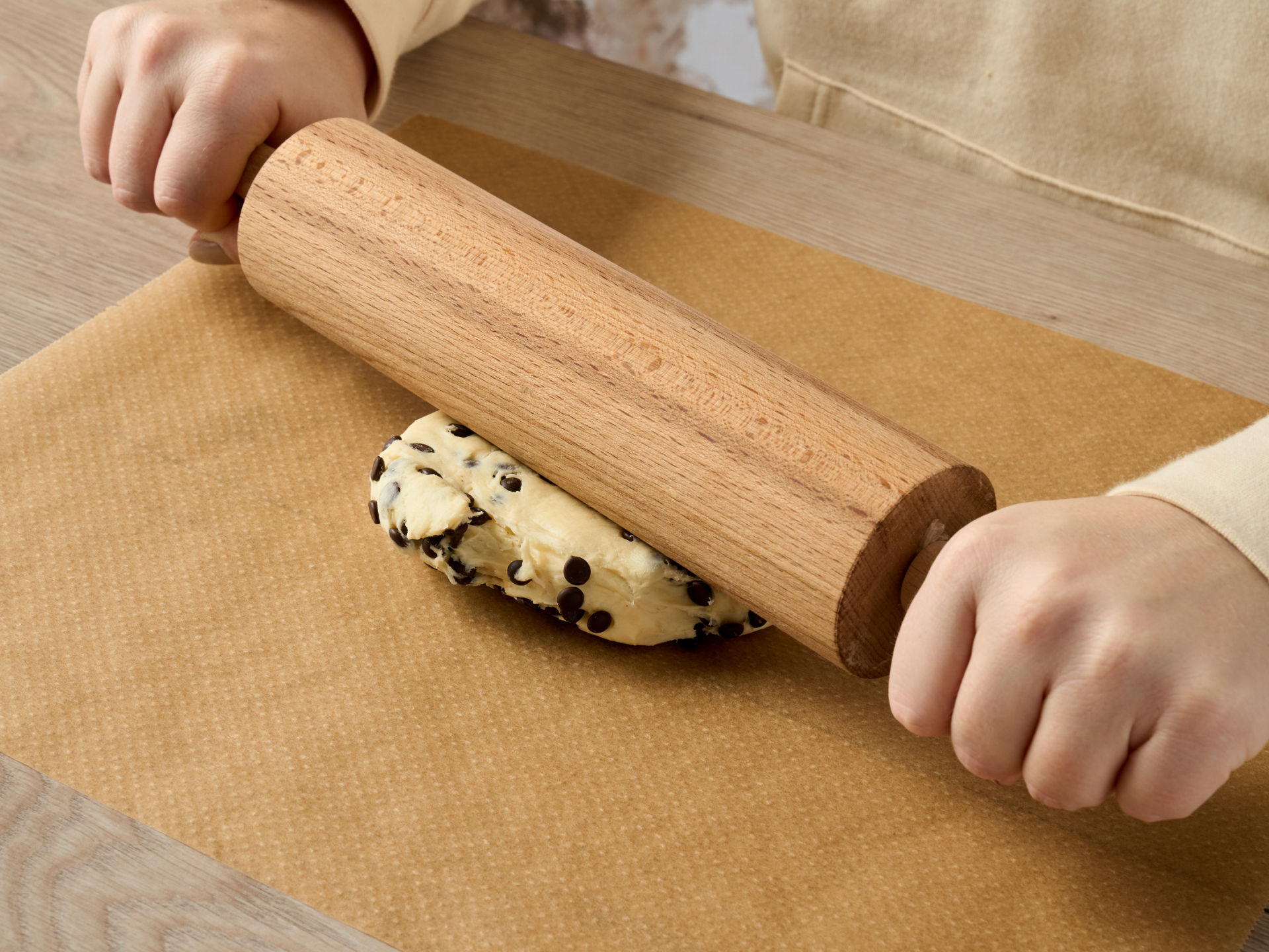 Teig mit Schokoladenstückchen wird auf Backpapier mit einem Nudelholz ausgerollt.