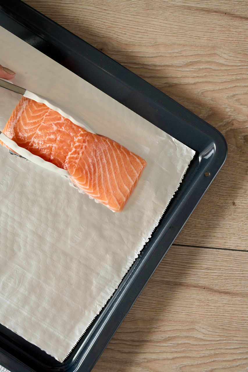 en stuk verse zalm wordt voorzichtig op een vel bakpapier gelegd dat op een bakplaat ligt, klaar om te worden bereid.