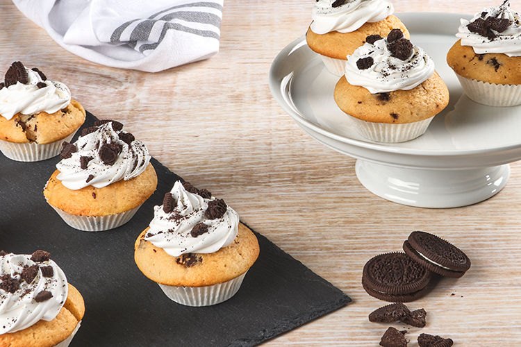 Cupcakes met witte topping en stukjes koek in Toppits bakvormpjes, op een schaal en een leisteen.