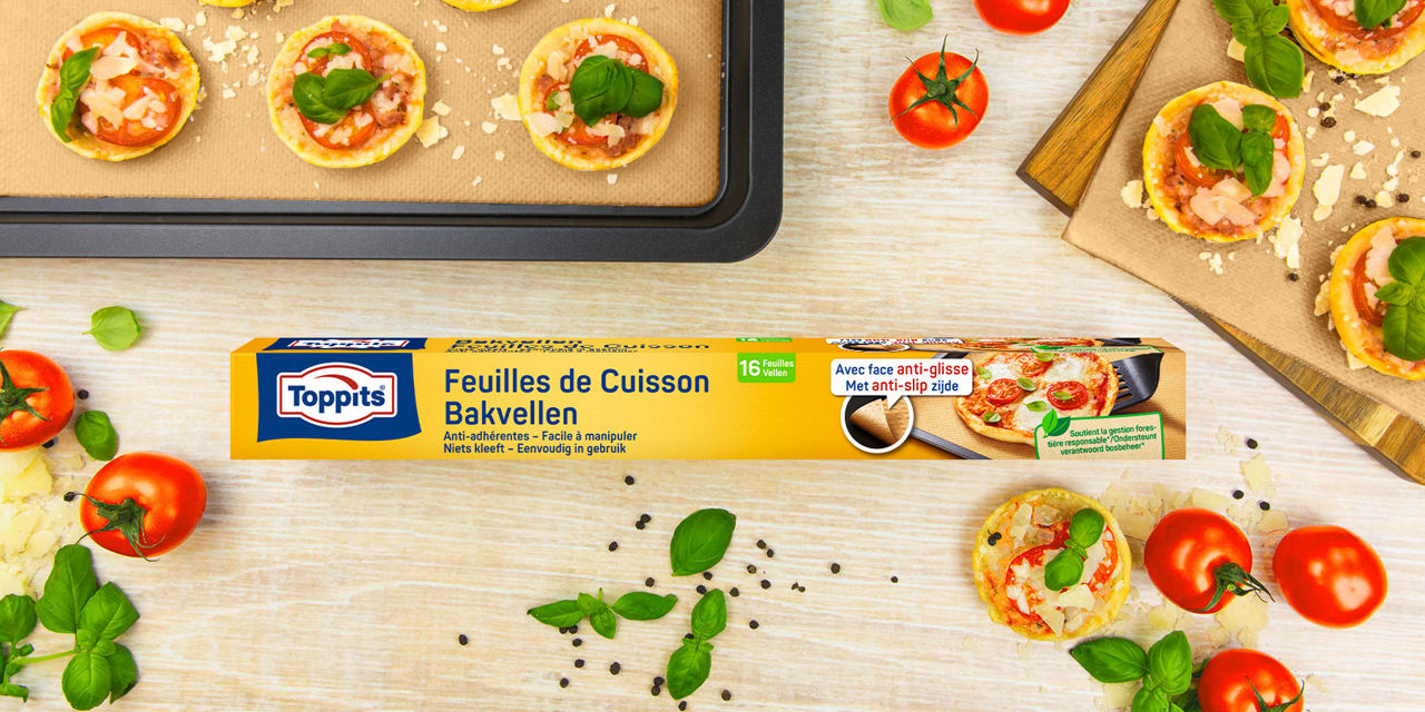 Een verpakking Toppits bakvellen ligt centraal op een tafel, omringd door mini pizza’s met basilicum, tomaat en kaas, en verse ingrediënten zoals tomaten en basilicum.