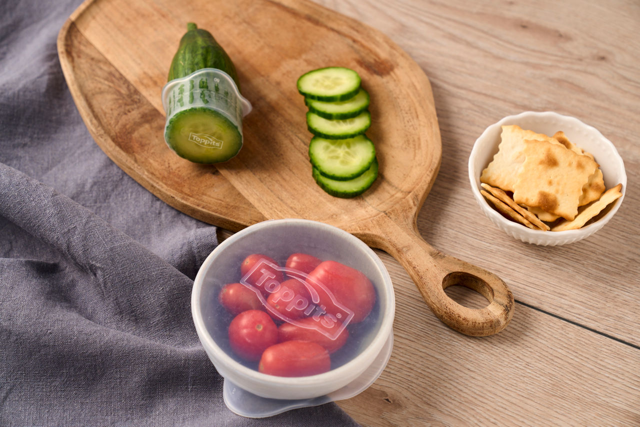 Un bol de tomates et un concombre tranché sont recouverts de couvercles en silicone de® Toppits