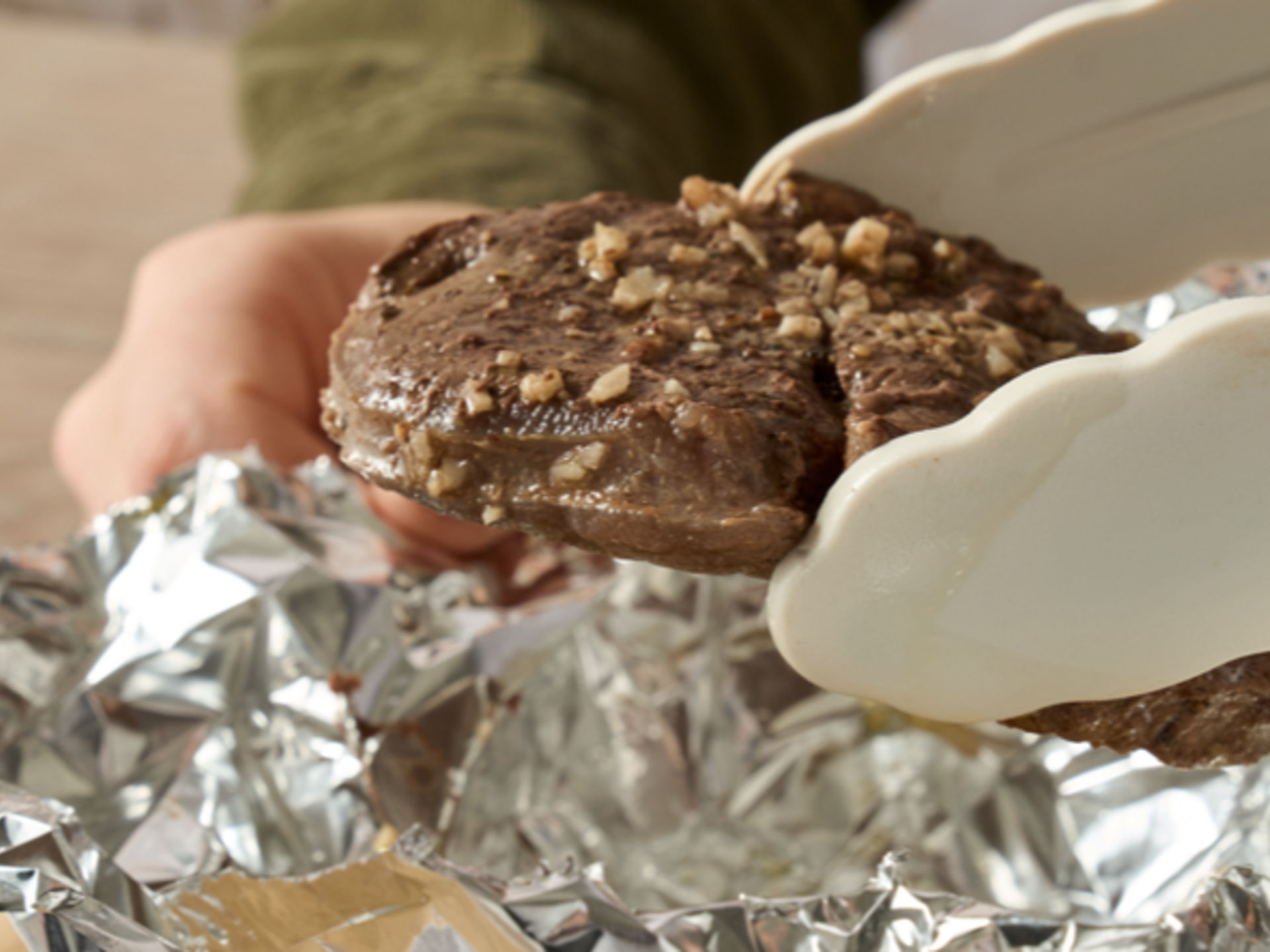 Ein gegartes Steak mit Gewürzen wird mit einer Grillzange aus Toppits Alufolie genommen  