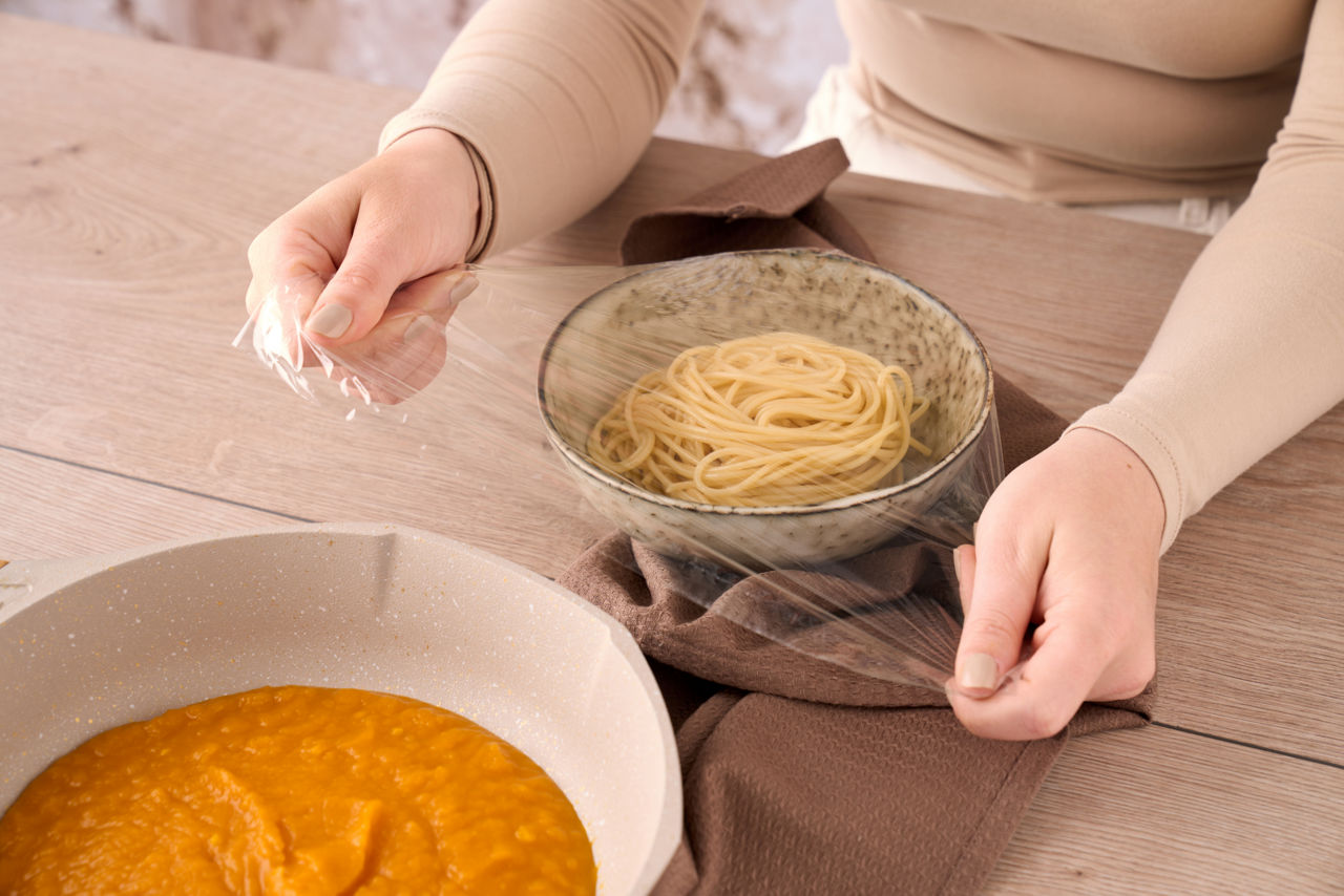Hände decken eine Schüssel mit Spaghetti mit Toppits Frischhaltefolie ab.