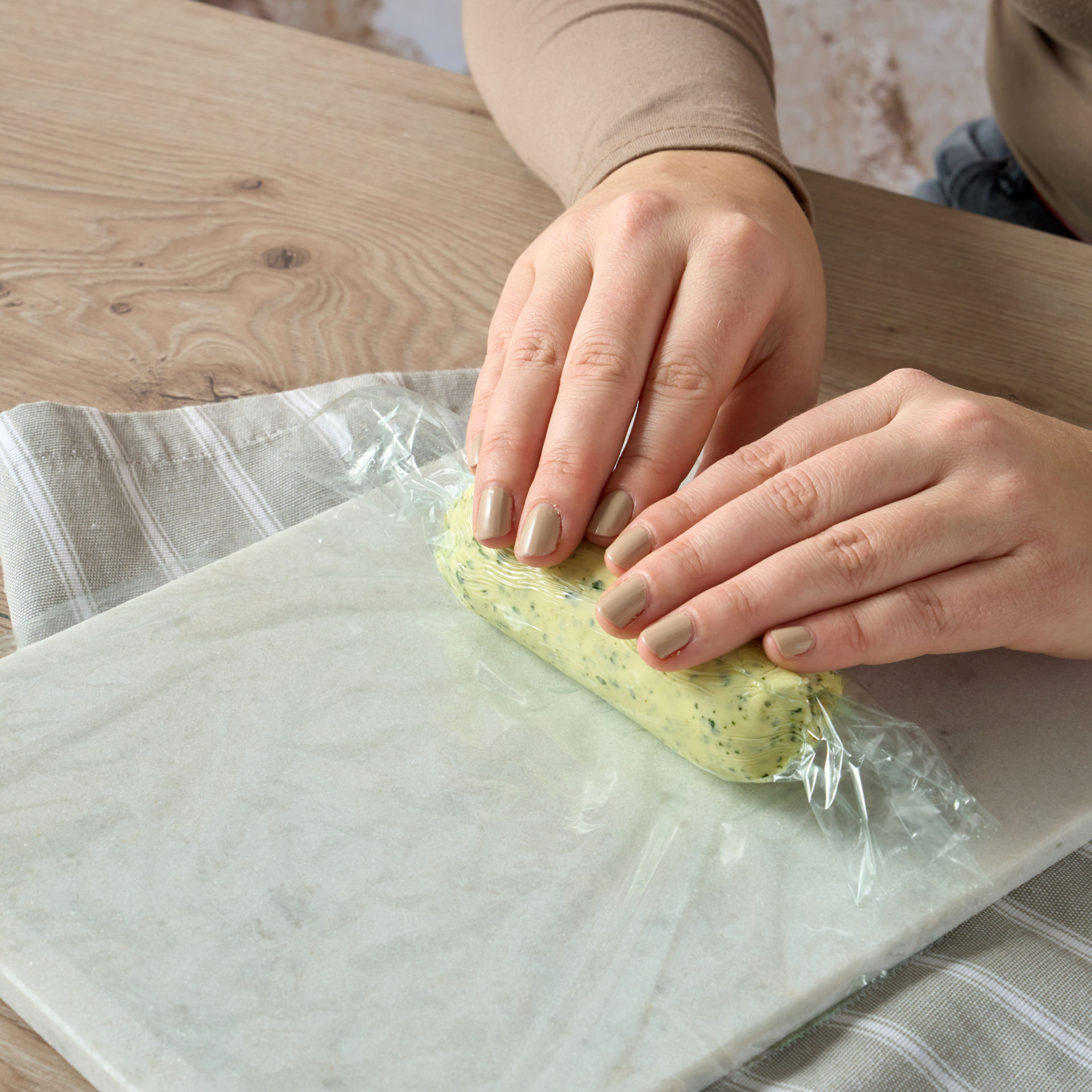 Person rollt Kräuterbutter in Toppits Frischhaltefolie auf einer Marmorplatte ein.