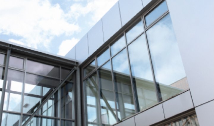 Moderne Glasfassade eines Büro- oder Industriegebäudes mit Spiegelung des Himmels in den Fenstern
