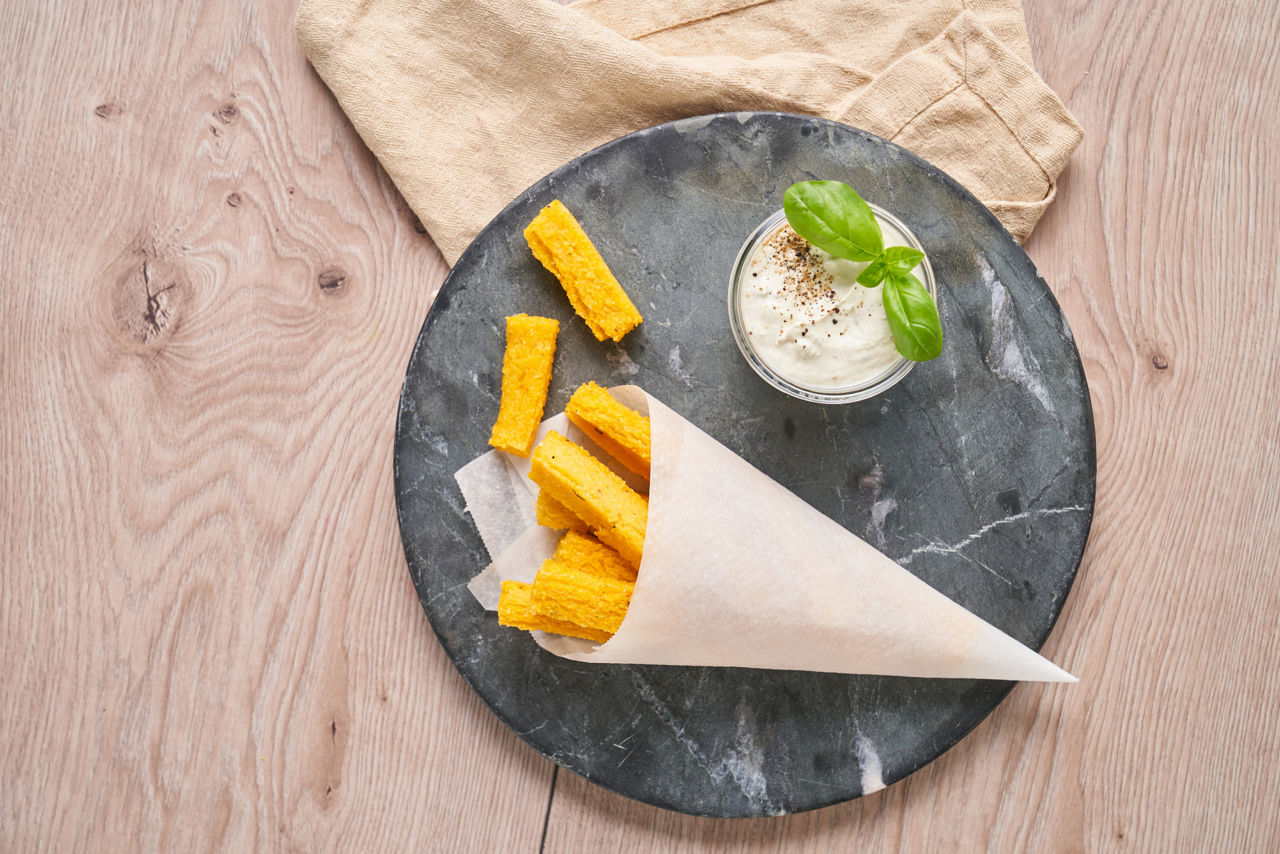 Polenta-Pommes in Pergamenttüte mit Dip auf schwarzem Servierstein, verfeinert mit Basilikum.