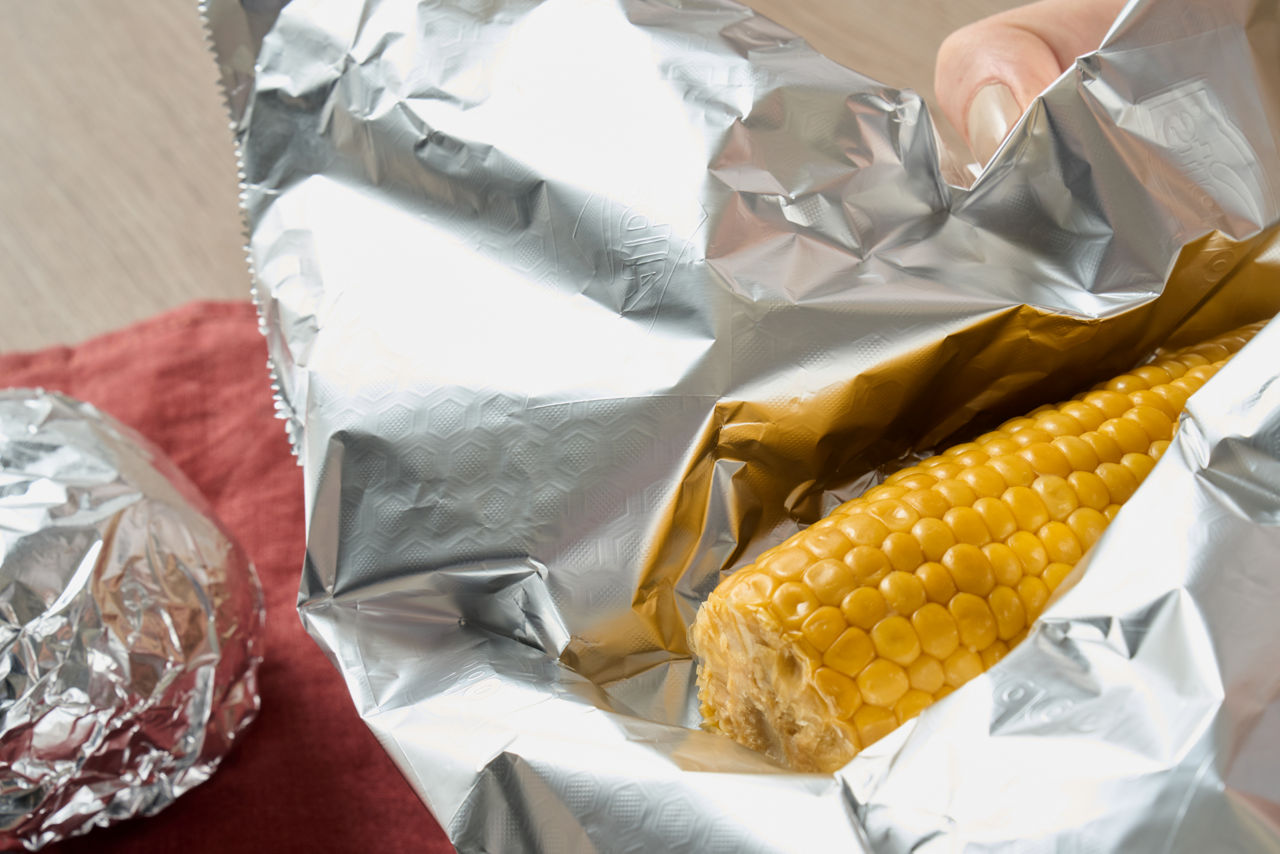 En majskolbe pakkes ind i aluminiumsfolie