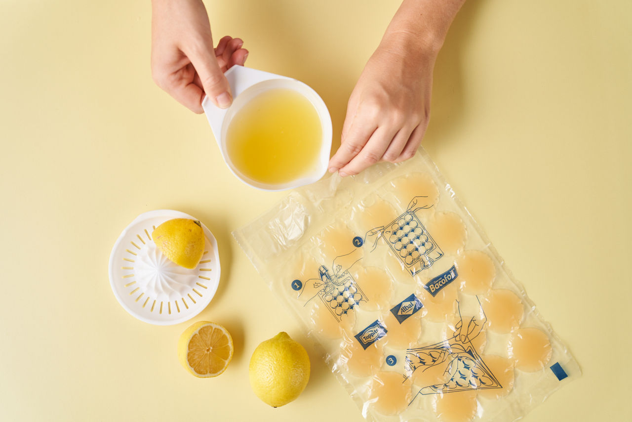 Hånd hælder citronsaft i Toppits® IceCubeBags på gul baggrund