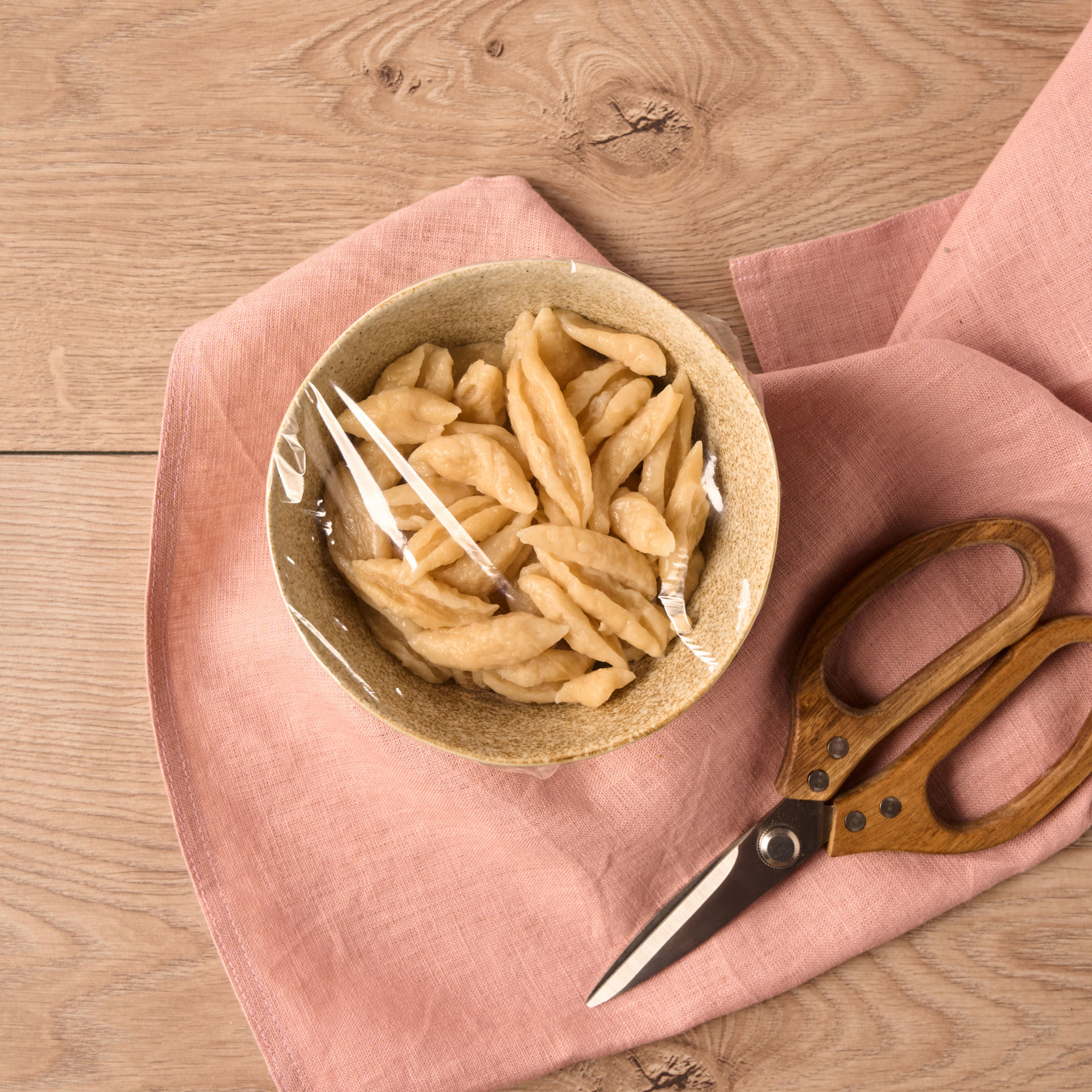 En skål med hjemmelavede nudler er dækket med Toppits® mikrobølgefolie 2-i-1, og der ligger en saks ved siden af