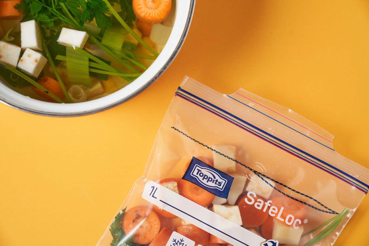 Toppits® SafeLoc® pose med skåret suppegrøntsager, ved siden af en skål med kogt grøntsagssuppe