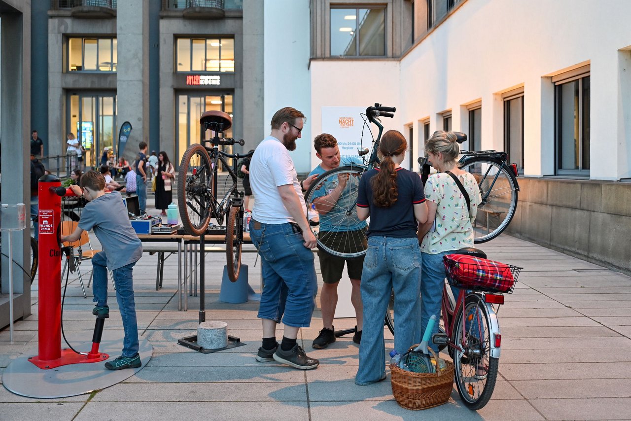 Eine Gruppe von Menschen steht um einen Fahrrad-Reparaturstand auf dem Museumsplatz, ein Kind benutzt eine Luftpumpe, im Hintergrund weitere Besucher