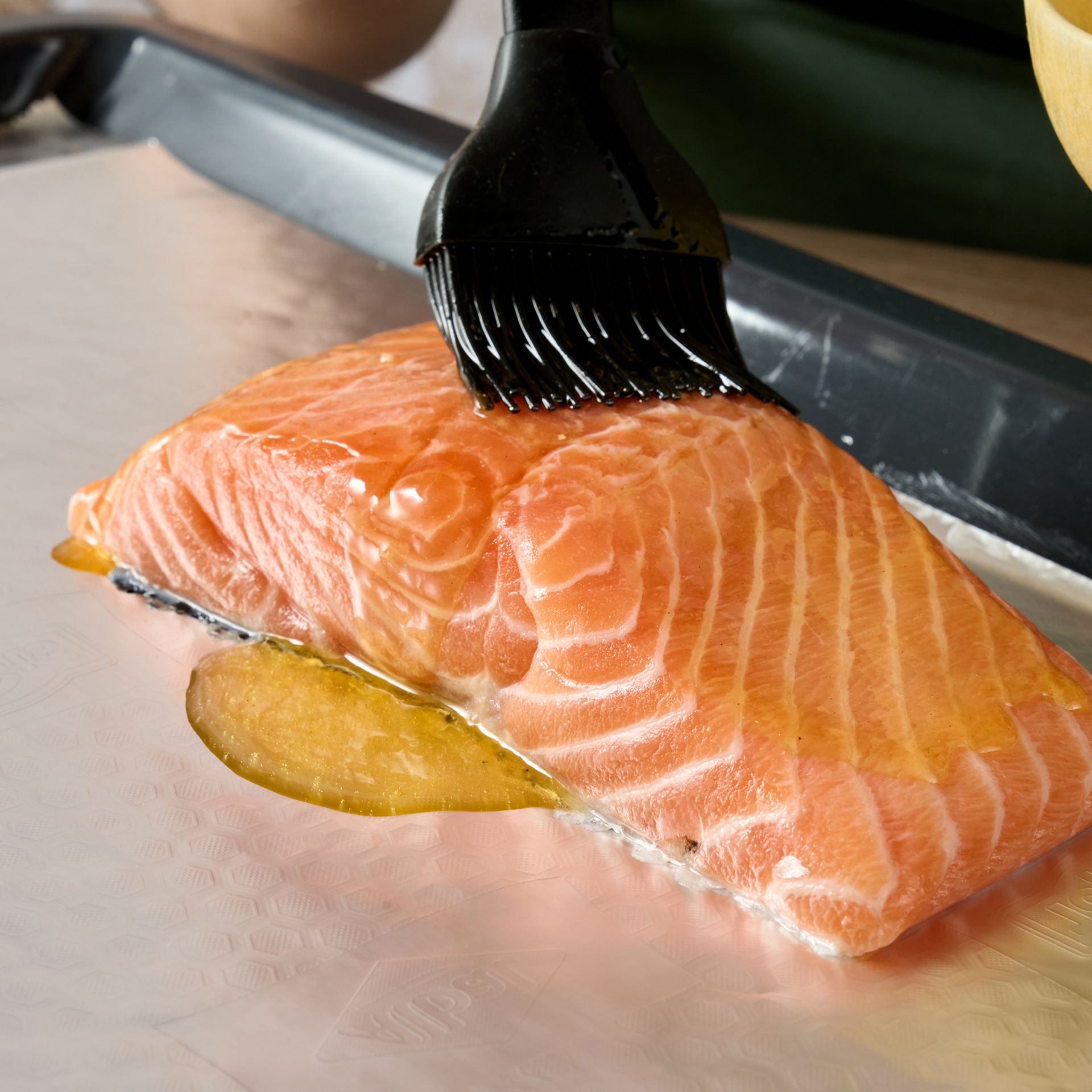 Filete de salmón siendo pincelado con salsa sobre papel de aluminio con textura de panal en una bandeja.