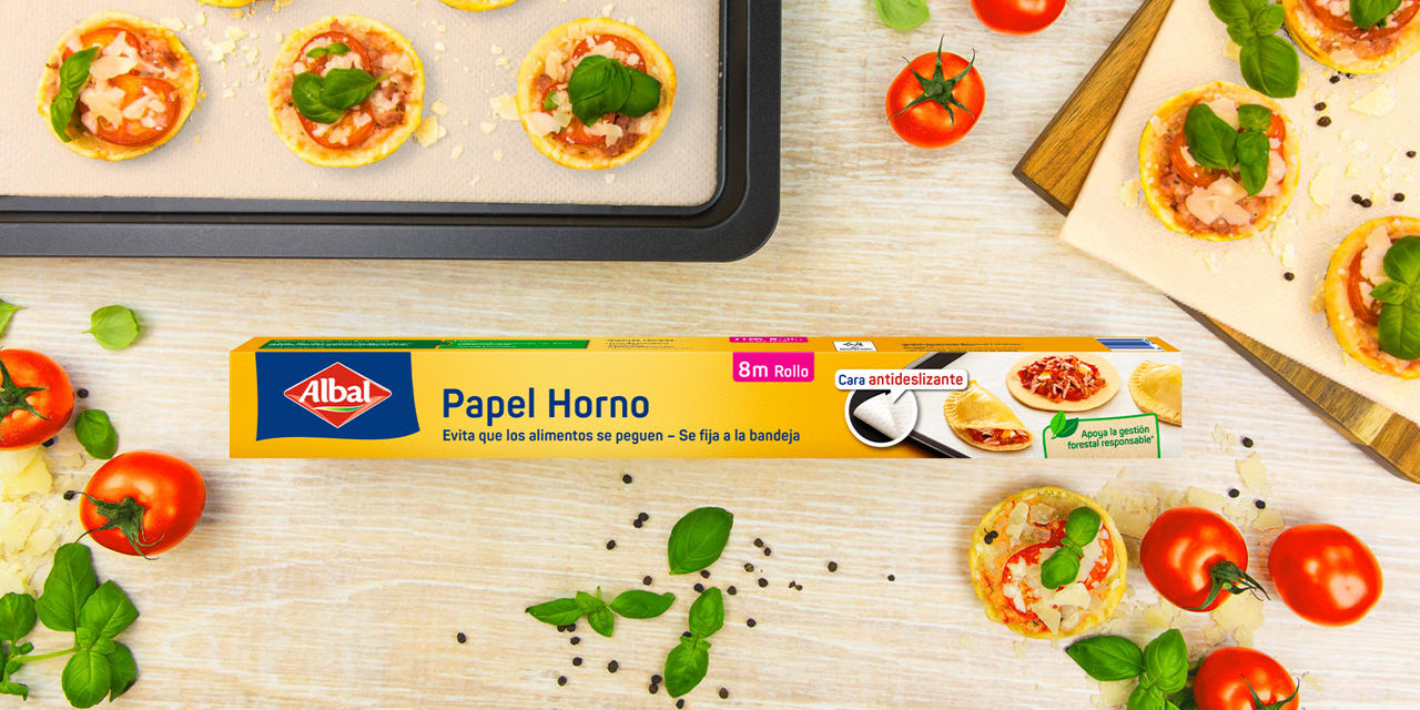 Caja de papel horno antiadherente de 8 metros rodeada de mini pizzas, tomates y albahaca fresca.