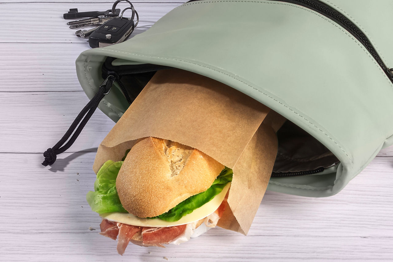 Bocadillo de jamón y queso envuelto en bolsa de papel sobresaliendo de una mochila verde, junto a unas llaves.