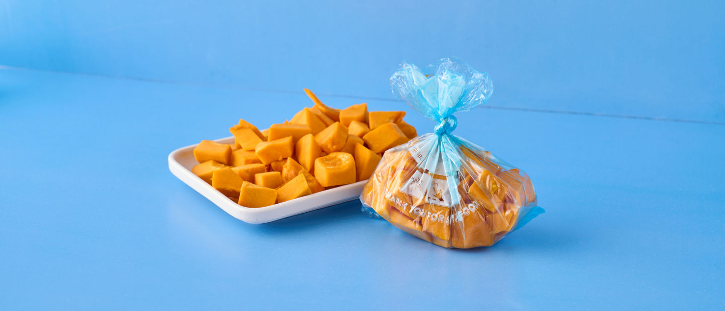 Sac de congélation Toppits® avec morceaux de courge, à côté des morceaux frais sur un plateau.