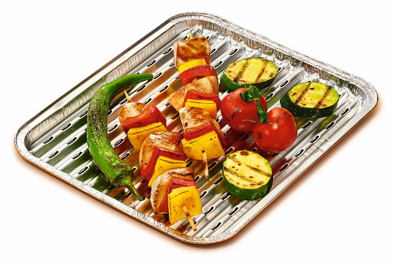 Eine Toppits Express Grillpfanne mit bunten Grillspießen aus Fleisch, Paprika und Zwiebeln, dazu gegrillte Zucchinischeiben, Tomaten und eine grüne Paprika 