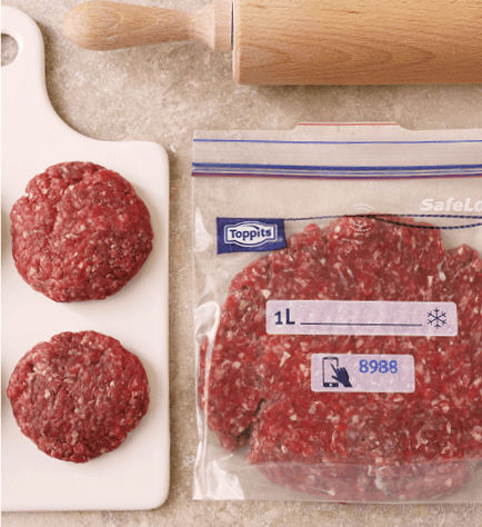 Flaches, rohes Hackfleisch in einem Toppits SafeLoc Gefrierbeutel neben geformten Hackfleisch-Patties auf einem Brett und einem Nudelholz.