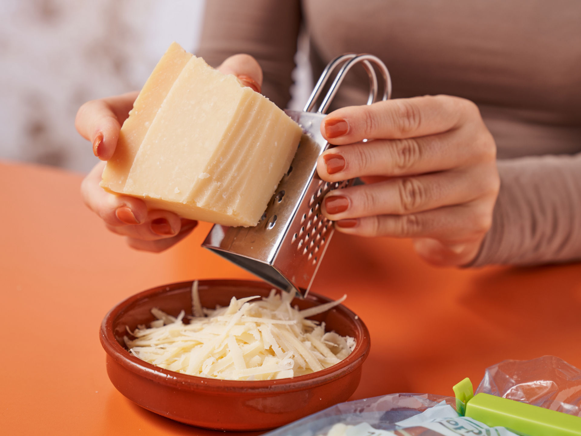 Geriebener Hartkäse fällt direkt in eine Schale, während er frisch geraspelt wird.