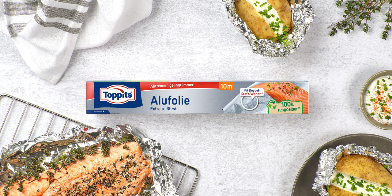 Toppits Alufolie (10 m) auf Tisch, umgeben von Folienkartoffeln und Lachs in Alufolie.