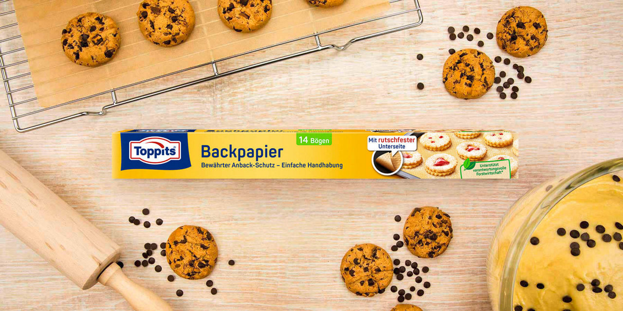 Toppits Backpapier 14 Bögen mit Schoko-Cookies, Schokotropfen und Backzubehör auf Holzunterlage.