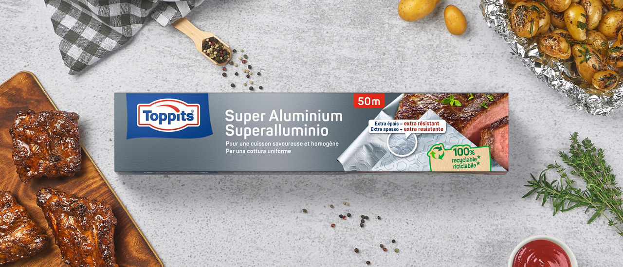 Verpakking van Toppits® Super aluminiumfolie op een lichte ondergrond, met daarnaast gegrild vlees, kruiden en specerijen 