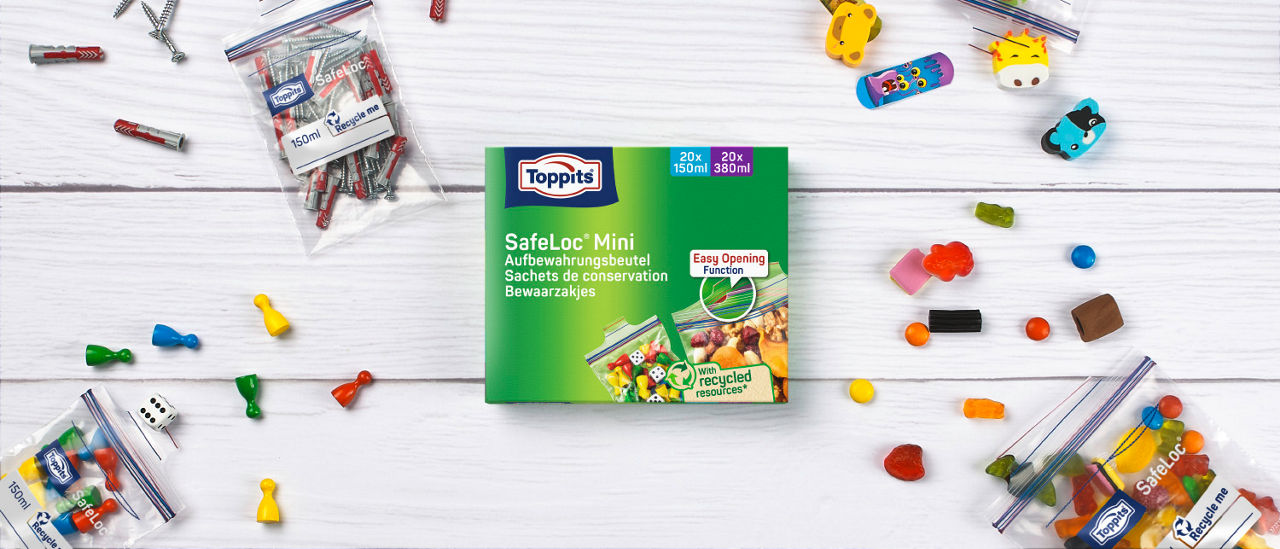 Toppits SafeLoc Mini Aufbewahrungsbeutel-Packung auf einem weißen Tisch, umgeben von kleinen Beuteln mit Schrauben, Spielfiguren und Süßigkeiten