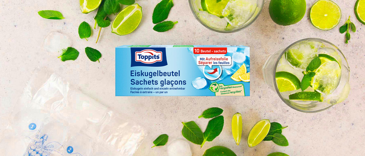 Toppits Eiskugelbeutel (10 Stück) auf Tisch, umgeben von Limetten, Minze, Eiswürfeln und Gläsern mit Getränken.