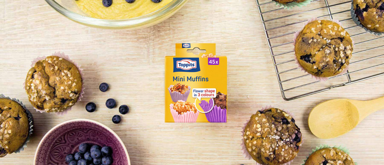 : Headerbillede med Toppits® Mini Muffins papirforme emballage og forme, dekoreret med muffins og ingredienser