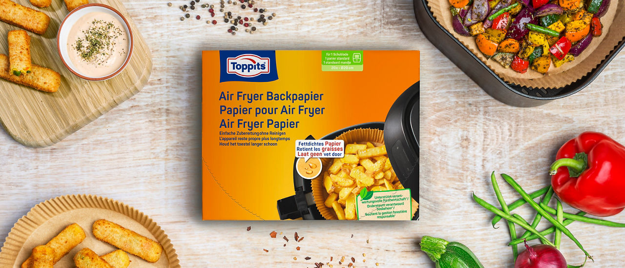 Verpakking Toppits Airfryer Papier tussen groenten, snacks en een airfryer met bakpapier en geroosterde groenten.